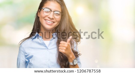 Young beautiful arab woman wearing glasses over isolated background doing happy thumbs up gesture with hand. Approving expression looking at the camera with showing success.