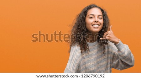 Beautiful young hispanic woman wearing stripes sweater smiling doing phone gesture with hand and fingers like talking on the telephone. Communicating concepts.