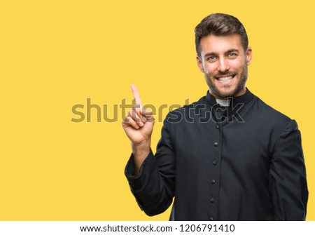 Young catholic christian priest man over isolated background with a big smile on face, pointing with hand and finger to the side looking at the camera.