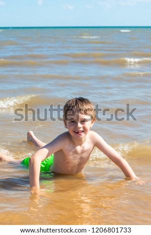 A handsome little boy with ADHD, Autism, Asperger Syndrome swimming, splashing water in the sea on a beautiful summers day, energetic