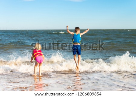 A handsome boy with ADHD, Autism, Asperger Syndrome plays with his sister swimming, splashing water in the sea on a beautiful summers day, energetic, wearing life jackets, buoyancy aids for safety