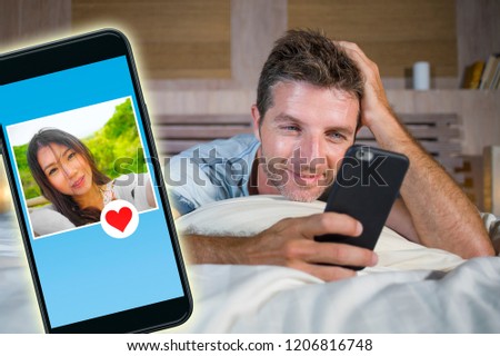 young handsome and happy man using internet social media on mobile phone searching love flirting and dating online sending like to beautiful Asian Chinese woman in technology romance concept