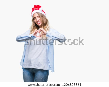 Beautiful young blonde woman wearing christmas hat over isolated background smiling in love showing heart symbol and shape with hands. Romantic concept.