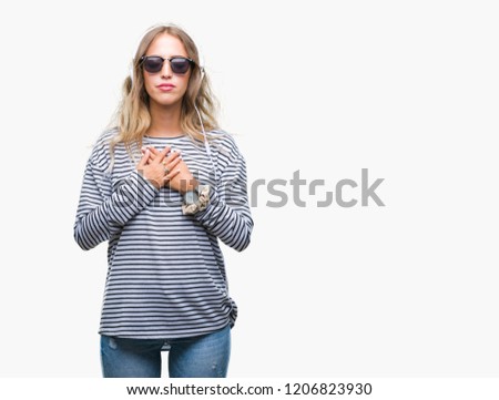 Beautiful young blonde woman wearing headphones and sunglasses over isolated background smiling with hands on chest with closed eyes and grateful gesture on face. Health concept.