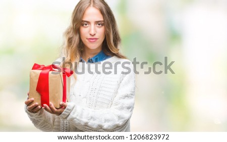 Beautiful young blonde woman holding gift over isolated background with a confident expression on smart face thinking serious