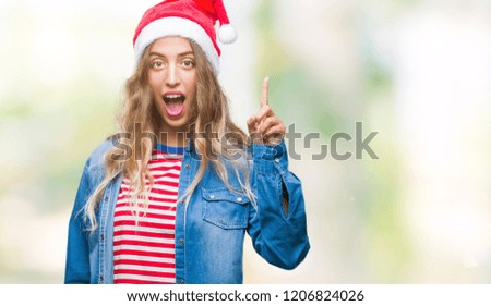 Beautiful young blonde woman wearing christmas hat over isolated background pointing finger up with successful idea. Exited and happy. Number one.