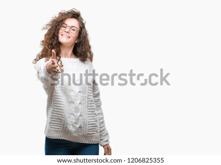 Beautiful brunette curly hair young girl wearing winter sweater over isolated background smiling friendly offering handshake as greeting and welcoming. Successful business.