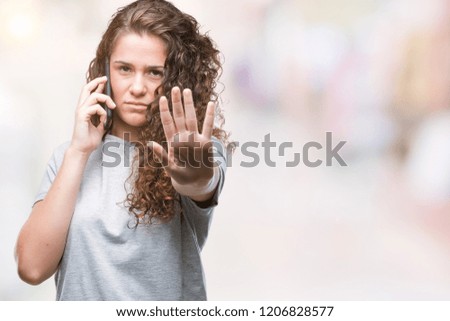 Young brunette girl talking on smartphone over isolated background with open hand doing stop sign with serious and confident expression, defense gesture