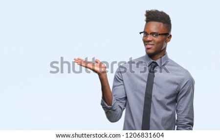 Young african american business man over isolated background smiling cheerful presenting and pointing with palm of hand looking at the camera.