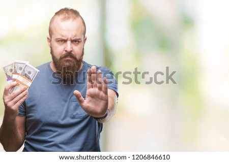 Young hipster man holding bunch of money over isolated background with open hand doing stop sign with serious and confident expression, defense gesture