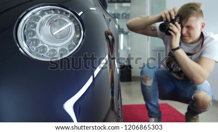 A young professional photographer (a guy, a man) takes pictures of a car in a car salon. Concept: lifestyle, new photo, car, photo camera, flash.