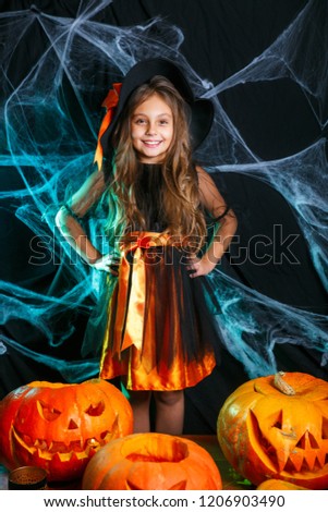 Happy Halloween. Little witch child having fun over spider web and with curved pumpkins background.