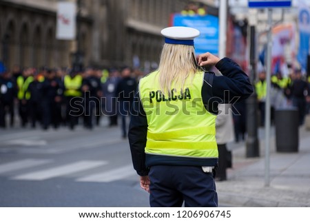 Police woman standing on the cross road and controlling the traffic. Dressed in a police uniform with yellow west. Royalty-Free Stock Photo #1206906745