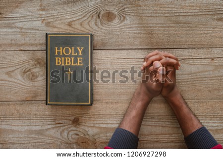 cropped shot of african american man sitting at rustic wooden table with holy bible