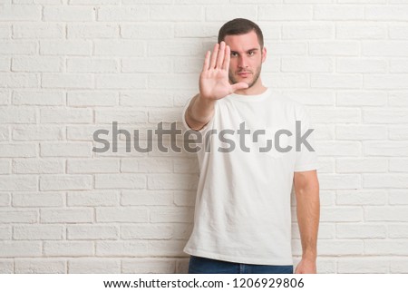 Young caucasian man standing over white brick wall smiling making frame with hands and fingers with happy face. Creativity and photography concept.