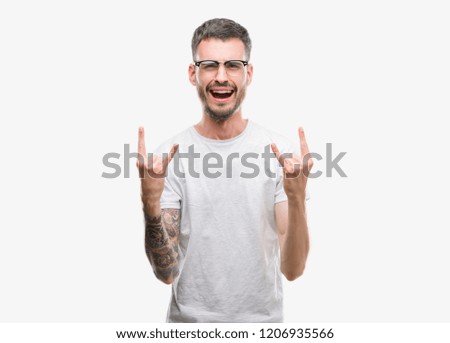 Young tattooed adult man shouting with crazy expression doing rock symbol with hands up. Music star. Heavy concept.