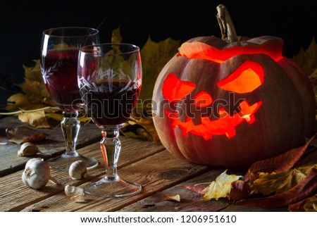 Halloween pumpkin with glasses of wine, garlic, and autumn leaves on old wooden boards. Background image to the Halloween holiday.