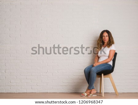 Middle age hispanic woman sitting on chair over white brick walll with a confident expression on smart face thinking serious Royalty-Free Stock Photo #1206968347