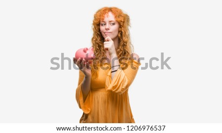 Young redhead woman holding piggy bank serious face thinking about question, very confused idea