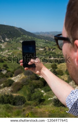 Male tourist and traveler in the mountains at the weekend travels with a telecommunication gadget. Makes landscape photos on your smartphone