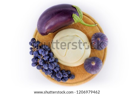 Violet still life with eggplant, soft cheese, fresh figs and a bunch of grapes on a wooden round board. White background top view 
