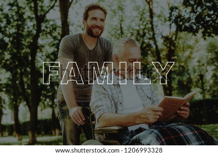 Reads a Book. Covered Rug. Sit. Wheelchair. Happy. Son and Old Man. Outdoor. Carry. Have Fun. Walking in Park. Assistance. Disabled. Rehabilitation. Therapy. Sunny. Road. Nursing Home. Handicapped.