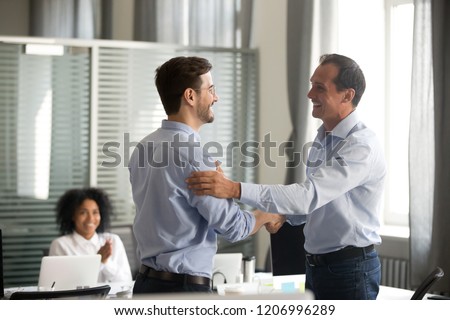 Smiling middle-aged ceo promoting motivating worker shaking hands congratulating with achievement promising respect bonus thanking for good work, team applauding, employee reward recognition concept Royalty-Free Stock Photo #1206996289