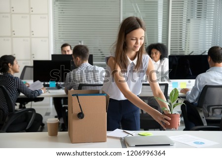 Smiling hired female company employee unpacking box with personal belongings at workplace on first working day in shared office, happy intern or newcomer got new job excited to start work concept Royalty-Free Stock Photo #1206996364