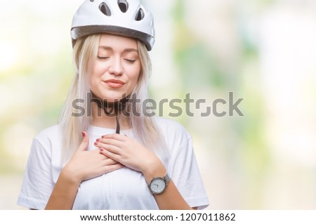 Young blonde woman wearing cyclist security helmet over isolated background smiling with hands on chest with closed eyes and grateful gesture on face. Health concept.