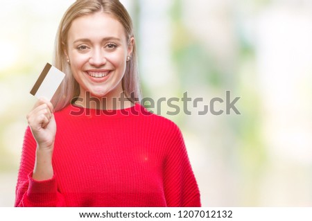 Young blonde woman holding credit card over isolated background with a happy face standing and smiling with a confident smile showing teeth