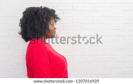 Young african american plus size woman over white brick wall looking to side, relax profile pose with natural face with confident smile.