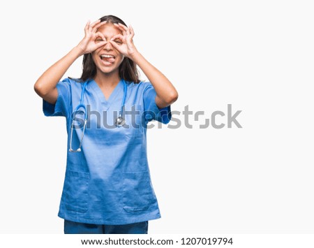 Young arab doctor surgeon woman over isolated background doing ok gesture like binoculars sticking tongue out, eyes looking through fingers. Crazy expression.
