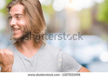 Young handsome man with long hair over isolated background holding football ball pointing and showing with thumb up to the side with happy face smiling