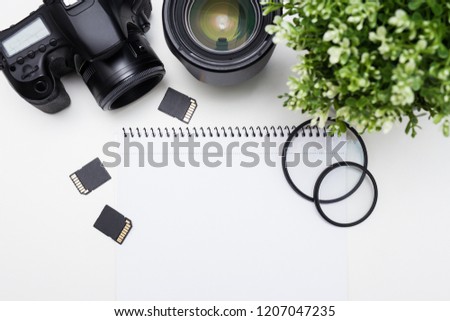 top view of photographer's workplace - camera, photography equipment and notepad over white table background