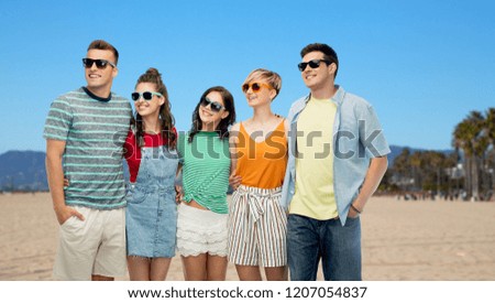 friendship, summer holidays and leisure concept - group of happy smiling friends in sunglasses hugging over venice beach background in california