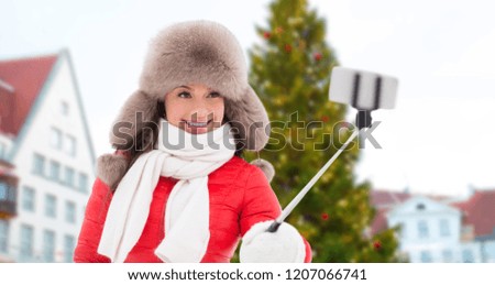people, season and leisure concept - happy smiling woman in winter fur hat taking selfie by smartphone over christmas tree at tallinn old town hall square background
