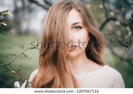 Portrait of beautiful plus size young woman posing in spring blossoming magnolia garden, creative film-like toning