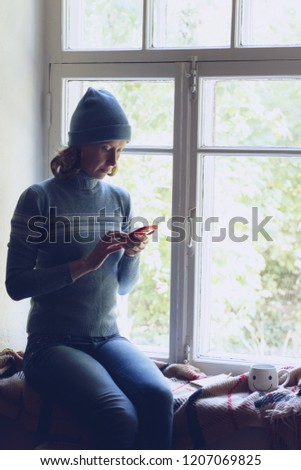 young woman sitting by the window using a smartphone