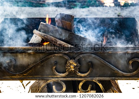 Metal grill, forged, handmade, with a pattern. A hot fire on the wood with smoke for barbecue and grilled products. Outside on a Sunny day.
