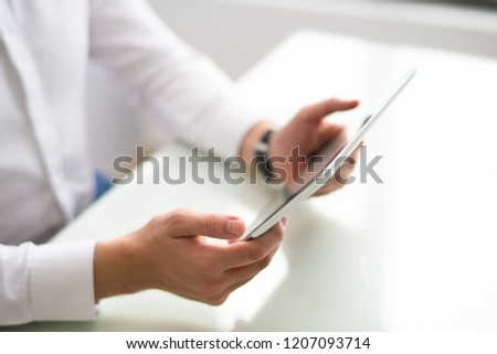 Close-up of unrecognizable man watching video on tablet. Businessman sitting at table and using modern device in office. Wi-fi technology concept