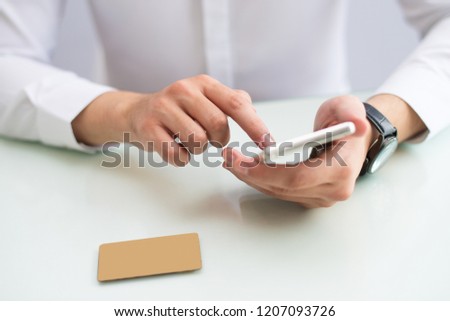 Close-up of unrecognizable entrepreneur checking finances while using online payment app on smartphone. Businessman sitting at table and reading information on phone. Browsing concept