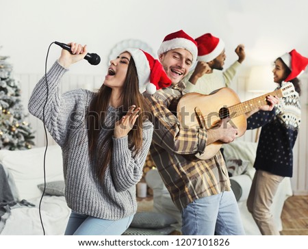 Happy couple playing on guitar and singing Christmas song at house party, copy space Royalty-Free Stock Photo #1207101826