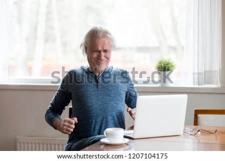 Exhausted aged man suffering from back pain sitting too long in incorrect posture, tired senior male stretch in chair working at laptop having body spasm or strain. Sedentary lifestyle problem concept Royalty-Free Stock Photo #1207104175