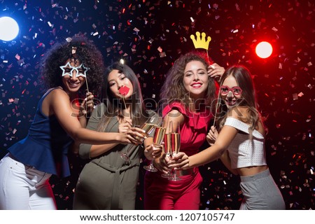 Fun at New Year party. Happy women celebrating and posing with photo props and champagne