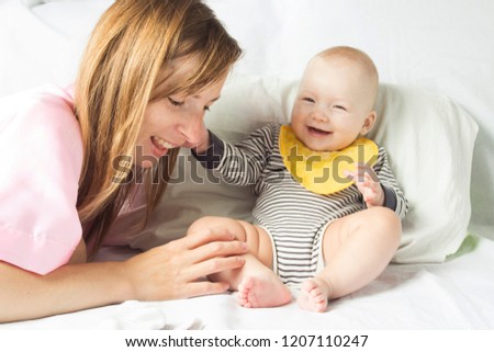 Young mother plays with a small child on a white bed after eatin