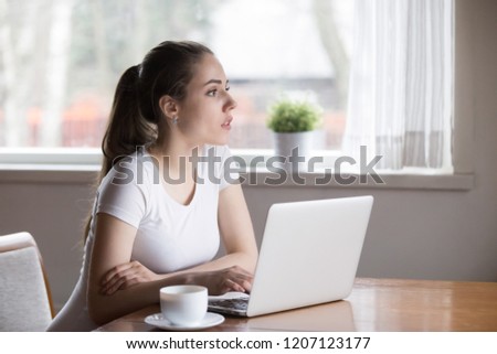 Pensive beautiful millennial woman writer sitting in kitchen at table thinking contemplating about new article for online journal. Thoughtful female using computer spend free time on weekend at home Royalty-Free Stock Photo #1207123177