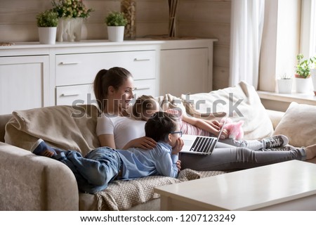 Loving mother resting relaxing with little preschool daughter and son together spend free time on weekend have fun using computer. Family surfing internet watch cartoons funny videos making video call