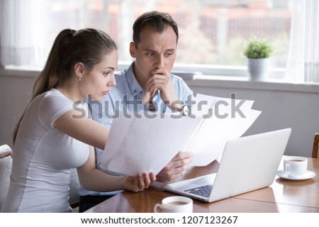 Stressed millennial married couple sitting at the desk at home use laptop checking documents unpaid bills, taxes, due debt, bank account balance. Bankruptcy lack of money financial problems concept Royalty-Free Stock Photo #1207123267