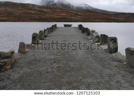 Stone pier in lake Bygdin in Norway, with snow covered mountains in the background