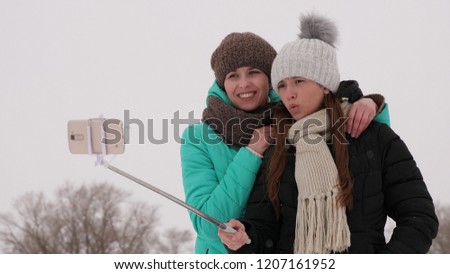 Mom and daughter do selphi Winter in snow. Carefree Teens Celebrate Christmas Outdoors, They Pose For Fun Selfies